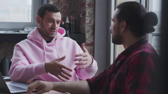 A Young Businessman with a Laptop Talks to a Colleague in the Office alt