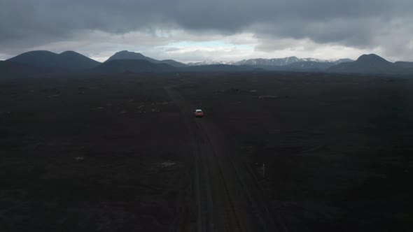 Birds Eye Off Road Car 4X4 Driving on Dirty Mountain Road Through Black Lava Sand Desert Landscape alt