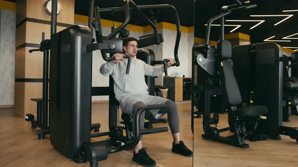 Young Man in Gray Hoodie Training Arms in a Gym