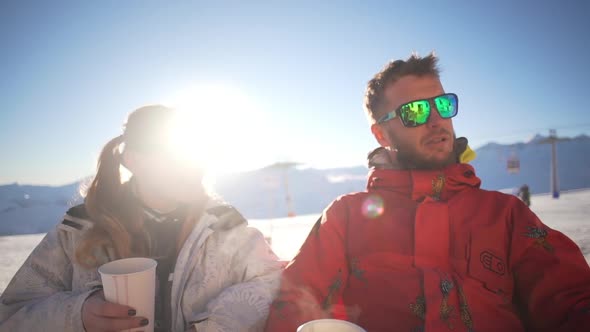 Caucasian Male Witn Beard and Mirrow Glasses Sitting and Talking with Female in Ski Mountain Resort alt