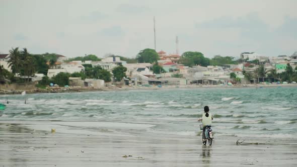 Little girl rides bicycle on Vietnamese seashore of Mui Ne beach, near fisherman village alt