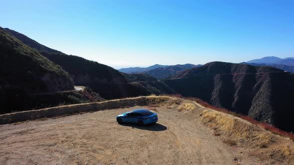 Flying slowly towards mountains and over a blue Tesla Model S on Mt. Baldy in Southern California. alt