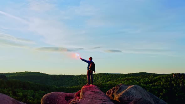 Aerial Shots of a Male Hiker Standing on Top with a Signal Light in His Hand alt