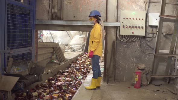 Womanworker in Yellow and Transparent Protecting Glasses Hard Hat and Mask Watching the Conveyor alt