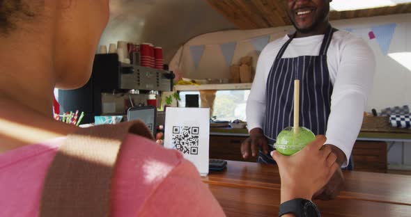 African american woman making payment from her smartphone by scanning the qr code at the food truck alt