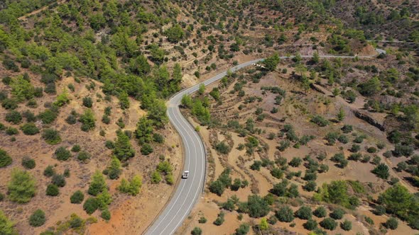 Car Drives on Winding Road Among Scrublands in Highland