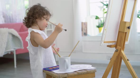 A little cute girl artist painting picture on canvas with watercolor paints at home	 alt