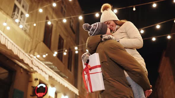 Young Woman Meeting Up With Boyfriend on Christmas Evening Party Hugging Tightly Together Swinging