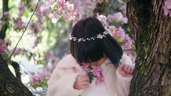 Korean Girl in a White Light Fur Coat and a Headband Sitting on a Tree Branch in a Garden with alt