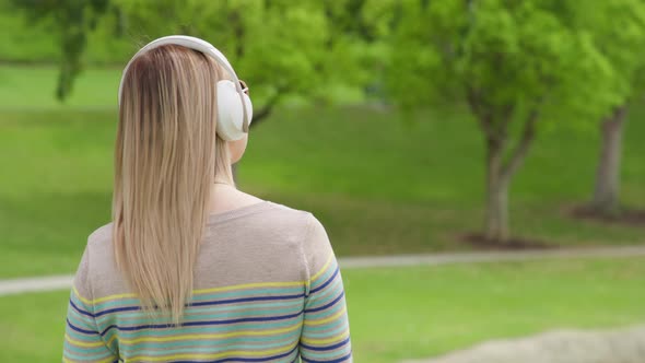 Positive Young Woman Listening Music in Wireless White Headphones in Green Park alt
