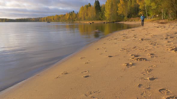 A Man Runs Along the Lake on a Sandy Beach. Early in the Morning at Dawn alt