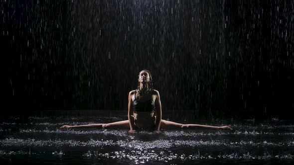 Under the Streams of Rain, a Young Woman Sits on a Twine and Enjoys an Exercise. Studio Light alt