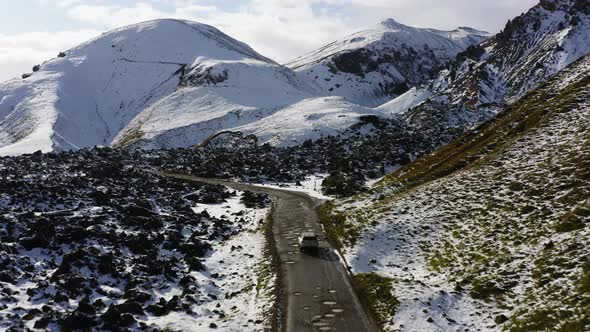 Aerial of Car Driving on Dirt Road Along the Snow Covered Mountains in Iceland alt