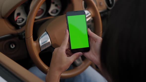 Woman Sits in Her Luxury White Convertible and Keeps Smartphone with Green Screen in Hands Next to