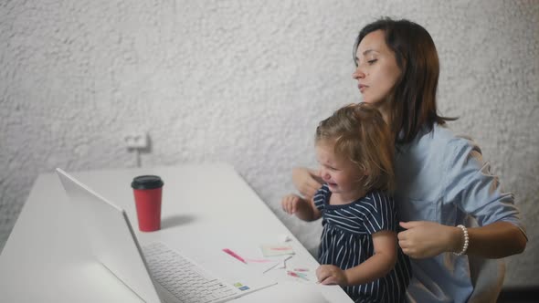 Woman Works in Office with a Naughty Child. Young Woman Calms Crying Child in Office. alt