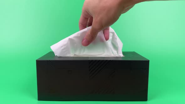 a person's hand pull out a piece of tissue from tissue paper box isolated on green background.