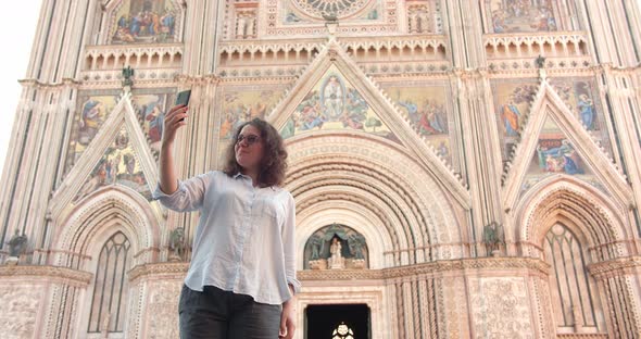 Young Caucasian female makes selfie in front of old cathedral in Italy