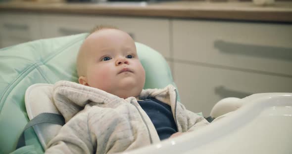 Funny Baby Relaxing Tapping His Little Palm on Feeding Chair and Briskly Eating alt