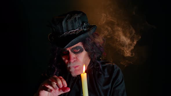 Sinister Man with Scary Halloween Witcher Makeup in Costume Making Voodoo Magic Rituals with Candle alt