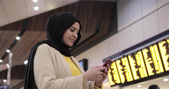 Smiling woman wearing hijab using smartphone at station