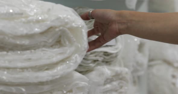 the girl runs her hand over the rolls of fabrics in the store and pulls out a large white roll alt