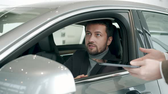 Car Buyer Talking To Dealer in Dealership Inside Shiny New Car Taking Key Fob alt