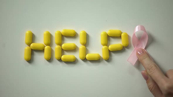 Woman Placing Pink Ribbon Near Help Word Made of Pills on Table, Breast Cancer alt