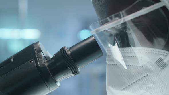 Black Lab Scientist in Protective Uniform Using Microscope alt