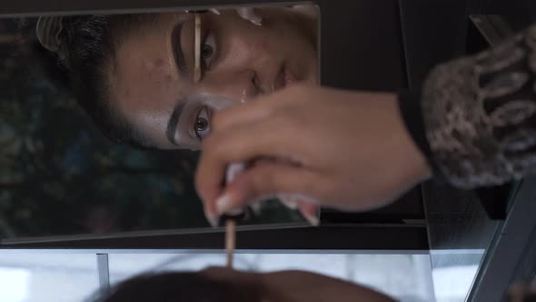 Young Woman Using Concealer To Shape Eyebrow Looking In Mirror. Vertical Video, Locked Off alt