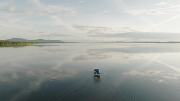 A motorboat putters along flat calm lake Ascending aerial shot alt