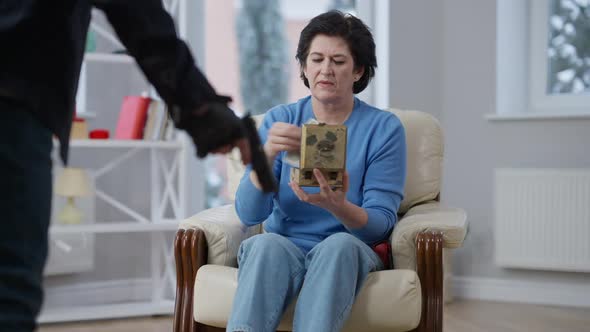 Panicked Caucasian Woman Giving Money to Unrecognizable Burglar Holding Gun alt