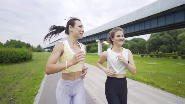 Smiling Female Run Along Track Together Near Bridge in Garden