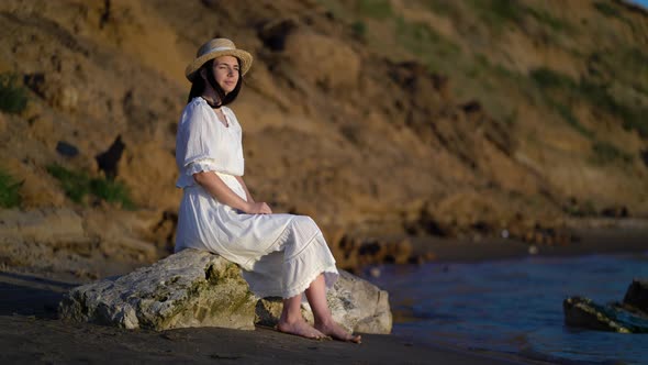 Woman in Dress Relaxing Sitting on a Big Stone in Sea alt