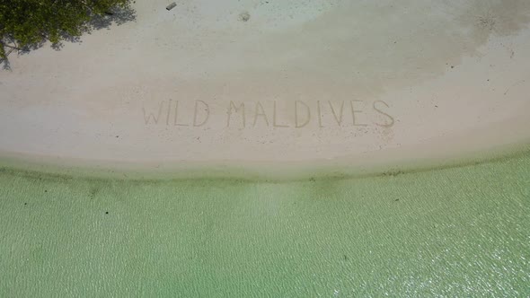 "Wild Maldives" inscription on the sand. Against the background of green trees, white sand, and the alt