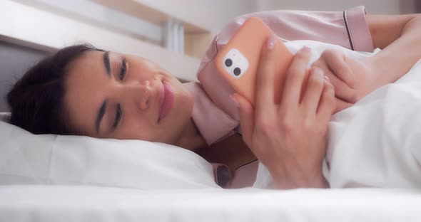 Woman Laughs After Reading a Message on Her Mobile Phone While Lying in Bed