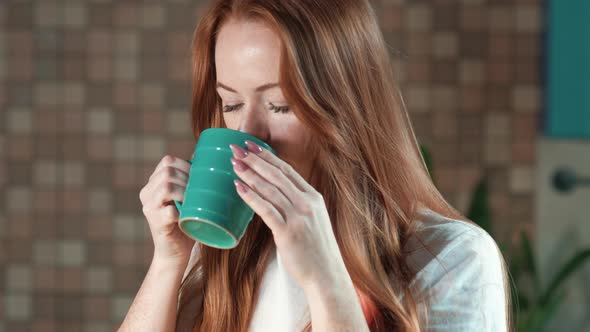 Caucasian woman enjoys drinking morning coffee from a cup in the home kitchen alt