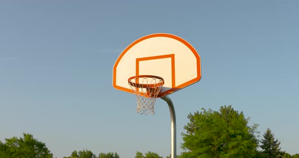 A low angle dolly towards a basketball net in the early morning sun. alt