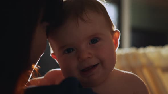 Happy Mother Holding Cute Newborn Baby in Cozy Dark Kids Bedroom in the Evening alt