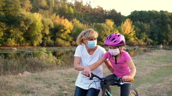 A young mother teaches his daughter to ride a Bicycle in medical masks and a Bicycle helmet