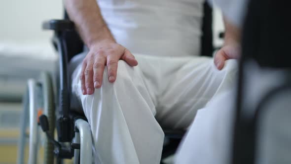 Unrecognizable Worried Man in Wheelchair Touching Legs Consulting Doctor in Hospital Indoors alt