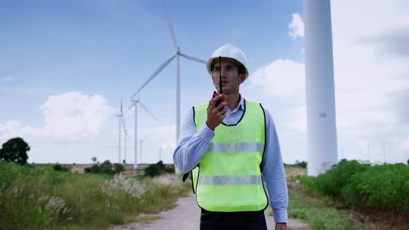 Asian male engineer using a radio to deliver work orders while inspecting a wind farm