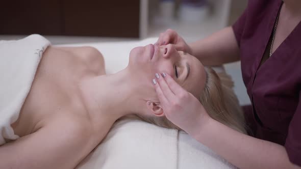 Hands of Professional Masseur Massaging Cheeks of Beautiful Woman with Closed Eyes alt