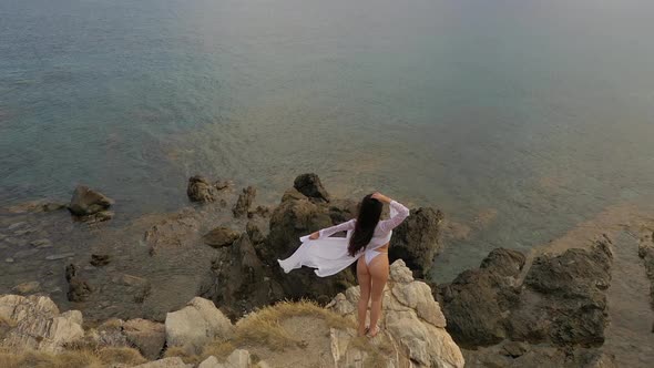 Young woman approaches edge of rocks admiring sunrise on sea