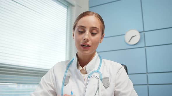 Blonde young woman medical blogger in white coat shows syringe alt