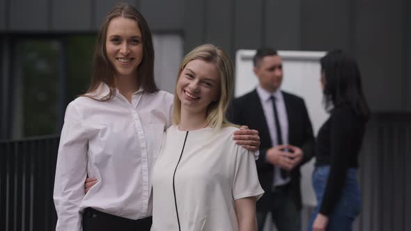 Happy Young Slim Beautiful Women Looking at Camera Smiling Hugging Standing Outdoors with Colleagues alt