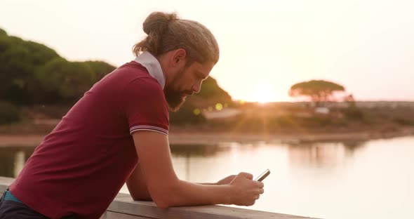 Side View of a Man Using His Gadget While Standing on the Bridge By the Pond alt