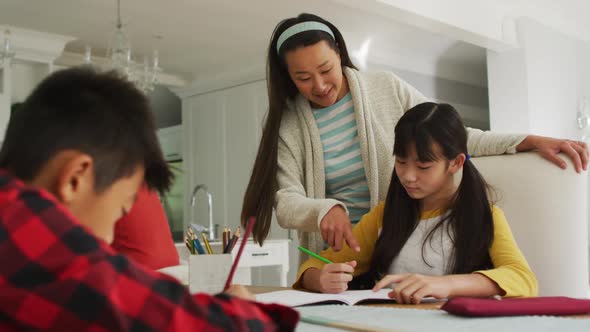 Asian mother in kitchen helping son and daughter doing schoolwork alt
