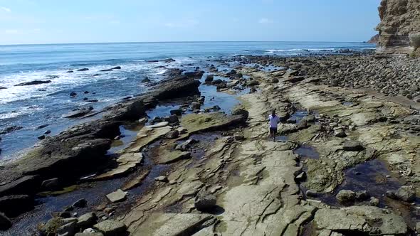 Tracking shot of a young man running on a rocky ocean beach shoreline alt