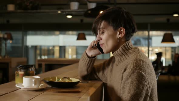 a Cute Girl in a Sweater Talking on the Phone Sitting in a Restaurant