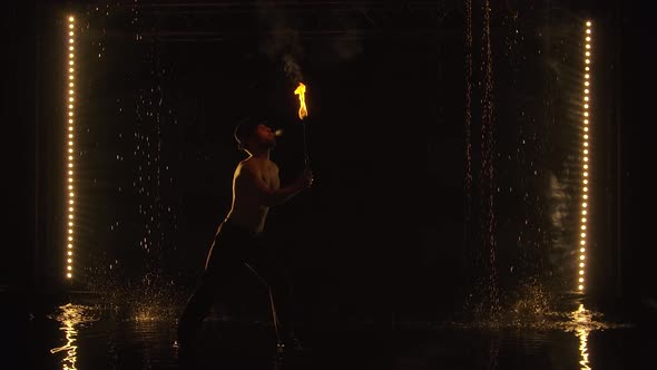 The Fakir Breathes Fire in a Dark Studio in the Rain. A Silhouette of a Half Naked Man alt